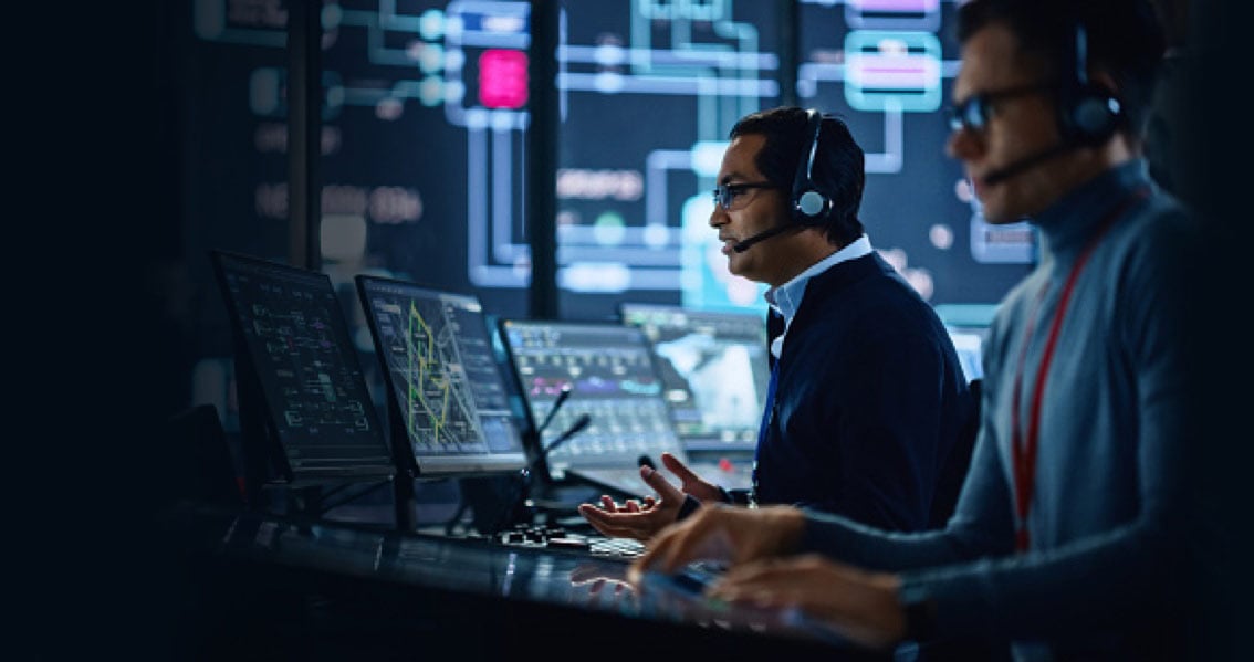 Zwei Männer mit Headsets arbeiten an mehreren Monitoren in einer SOC-Umgebung