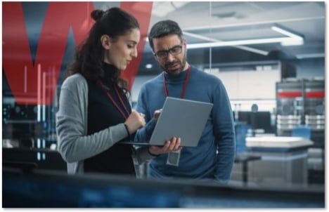 Co-workers looking at a laptop together standing in from of a large red W