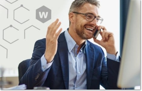 Man in a suit and glasses talking on the phone in front of his computer