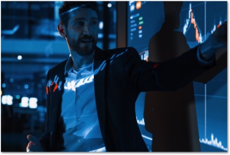 Man in a suit pointing at a chart projected in a dark room