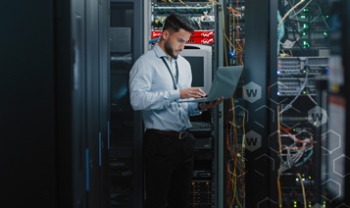Man working on a laptop in a server room with Red WatchGuard Fireboxes in the rack behind him