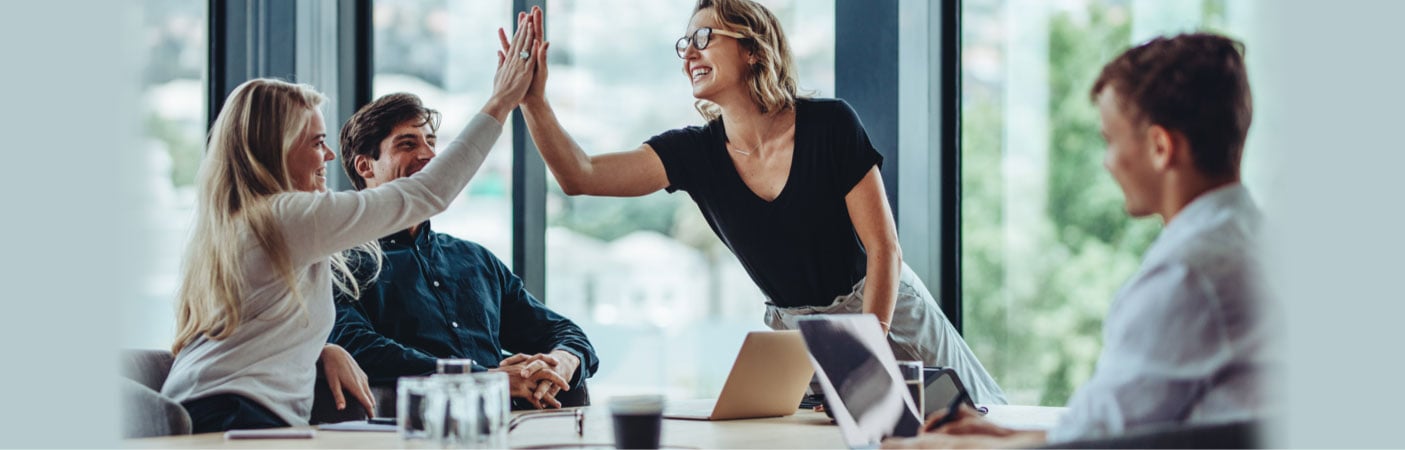 Two women high-fiving each other over a dining room table while two men look on